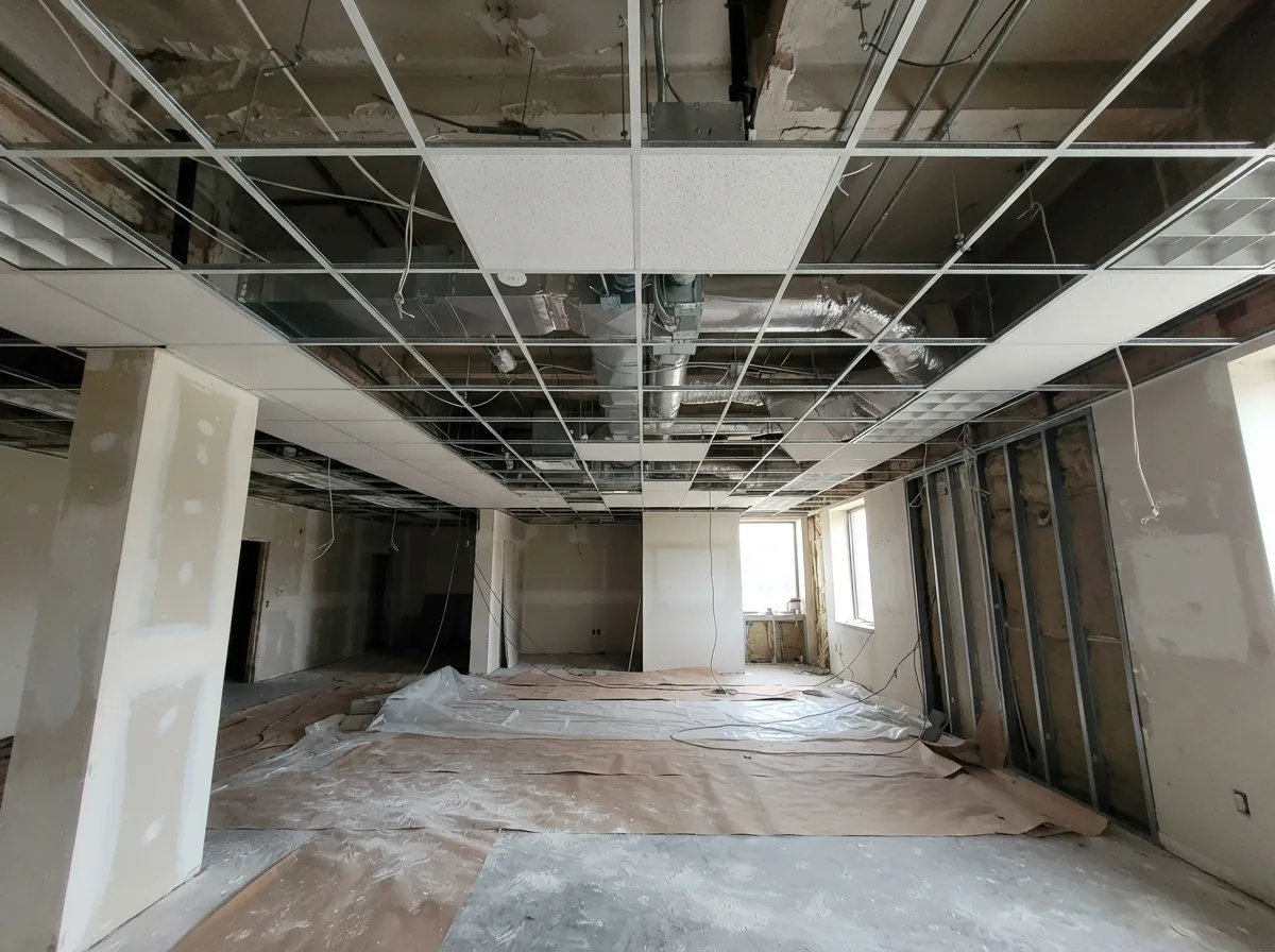 Suspended acoustical ceiling grid in an office under renovation, partly filled with white tiles, with ductwork visible through the open squares